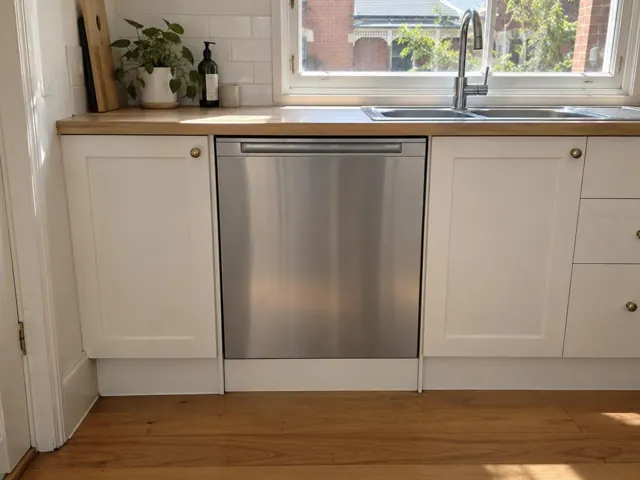 Dishwasher fitted under a timber benchtop in a white kitchen with a window in Islington