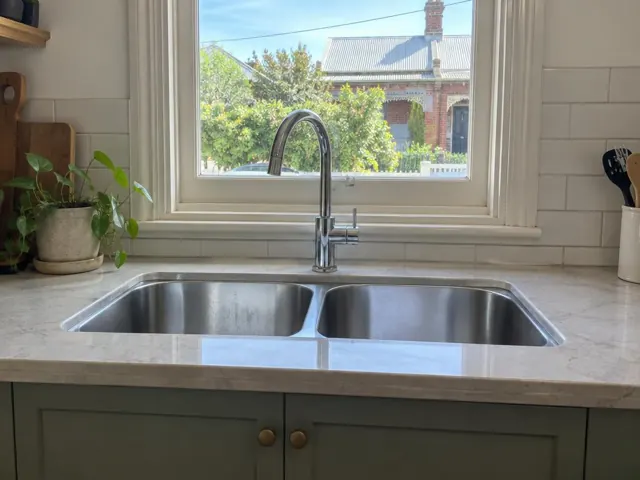 Stainless kitchen sink with chrome mixer tap below a window in a tiled home kitchen in Wickham
