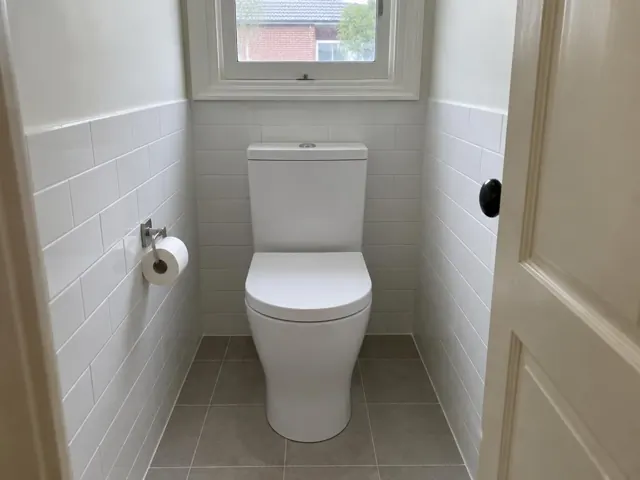 White toilet in a small tiled bathroom with window and door in Tighes Hill